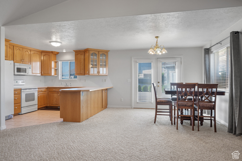 Kitchen featuring white appliances, light carpet, a peninsula, glass insert cabinets, and a chandelier