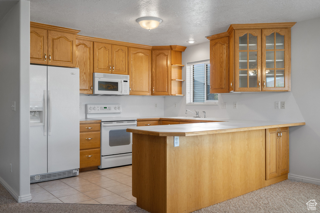Kitchen featuring white appliances, a peninsula, glass insert cabinets, light countertops, and a textured ceiling