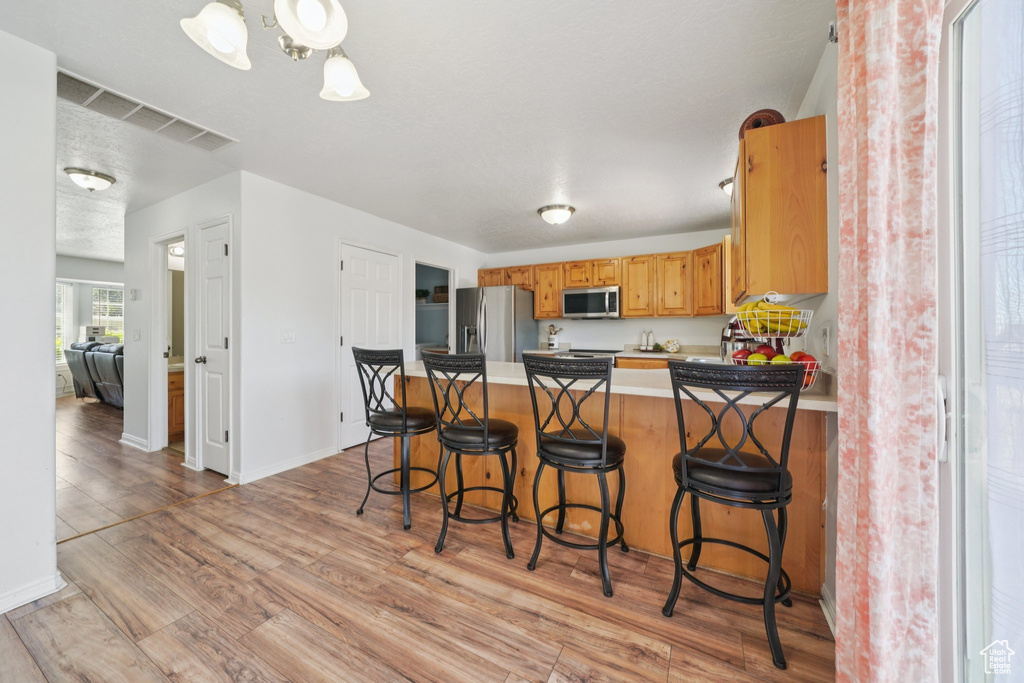 Kitchen featuring appliances with stainless steel finishes, a peninsula, light wood-style flooring, a breakfast bar area, and light countertops