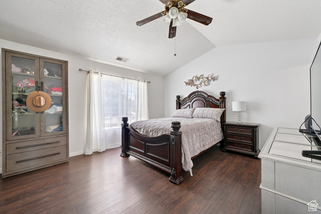 Bedroom featuring vaulted ceiling, dark wood-style floors, a ceiling fan, and a textured ceiling