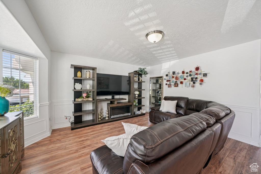 Living room with a textured ceiling, a wainscoted wall, wood finished floors, a fireplace, and a decorative wall