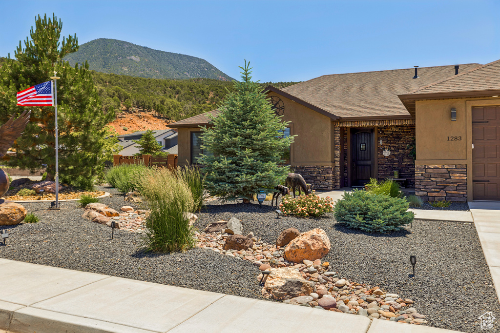 View of front of house featuring a mountain view, an attached garage, stone siding, and roof with shingles