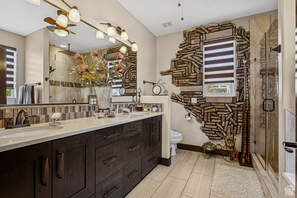Full bath featuring a ceiling fan, double vanity, a shower stall, and decorative backsplash