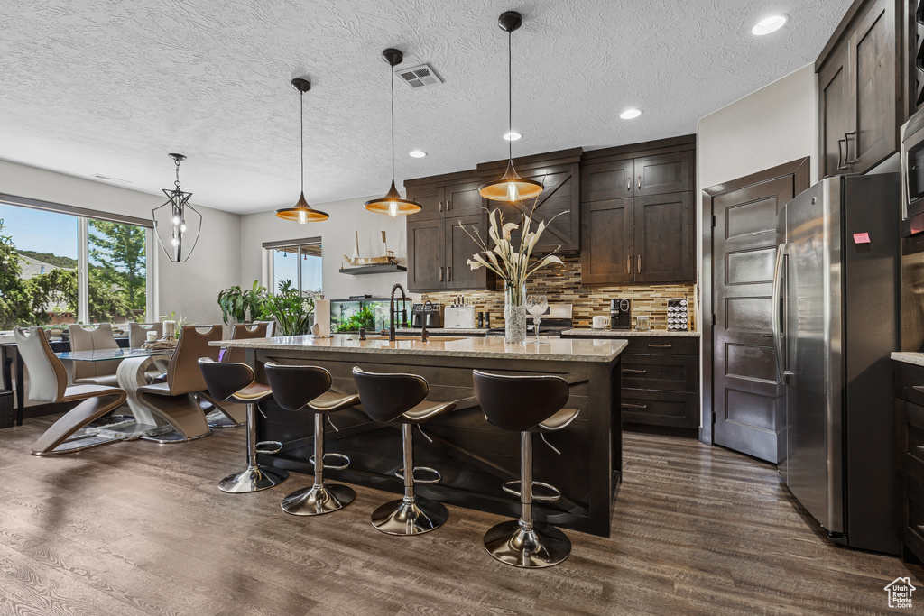 Kitchen featuring freestanding refrigerator, dark wood-type flooring, dark brown cabinets, tasteful backsplash, and a kitchen breakfast bar