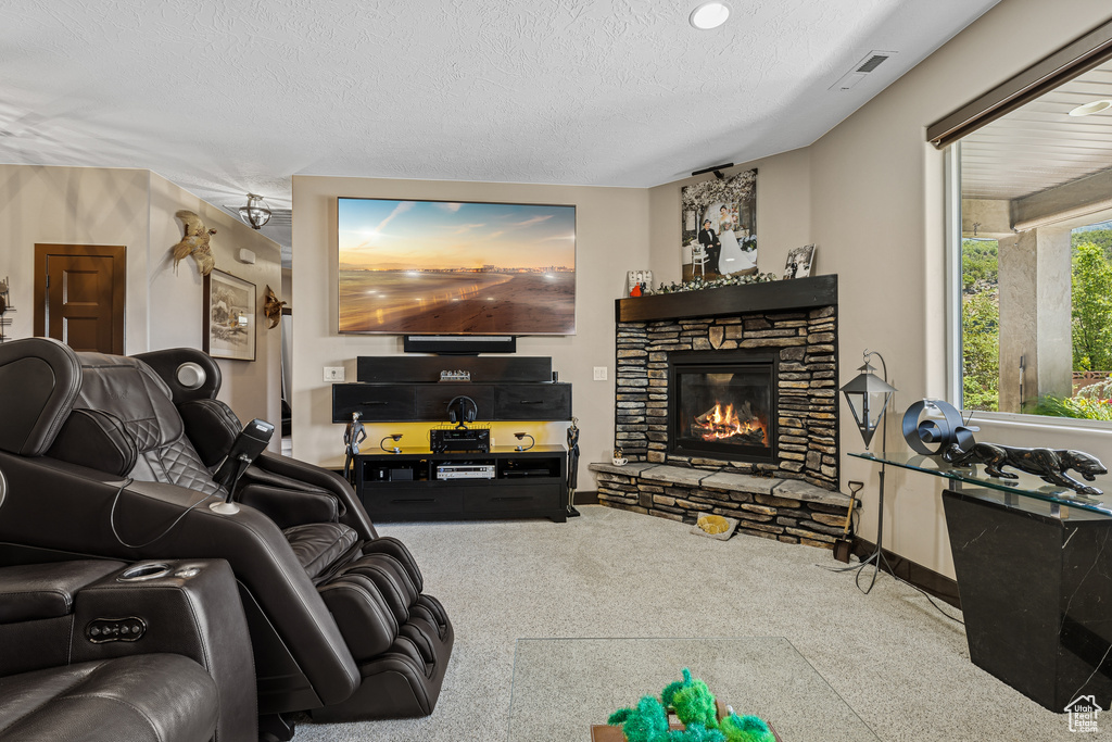 Living area with a textured ceiling, a stone fireplace, and carpet flooring