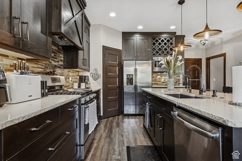 Kitchen featuring appliances with stainless steel finishes, wall chimney exhaust hood, backsplash, dark wood-style flooring, and light stone counters