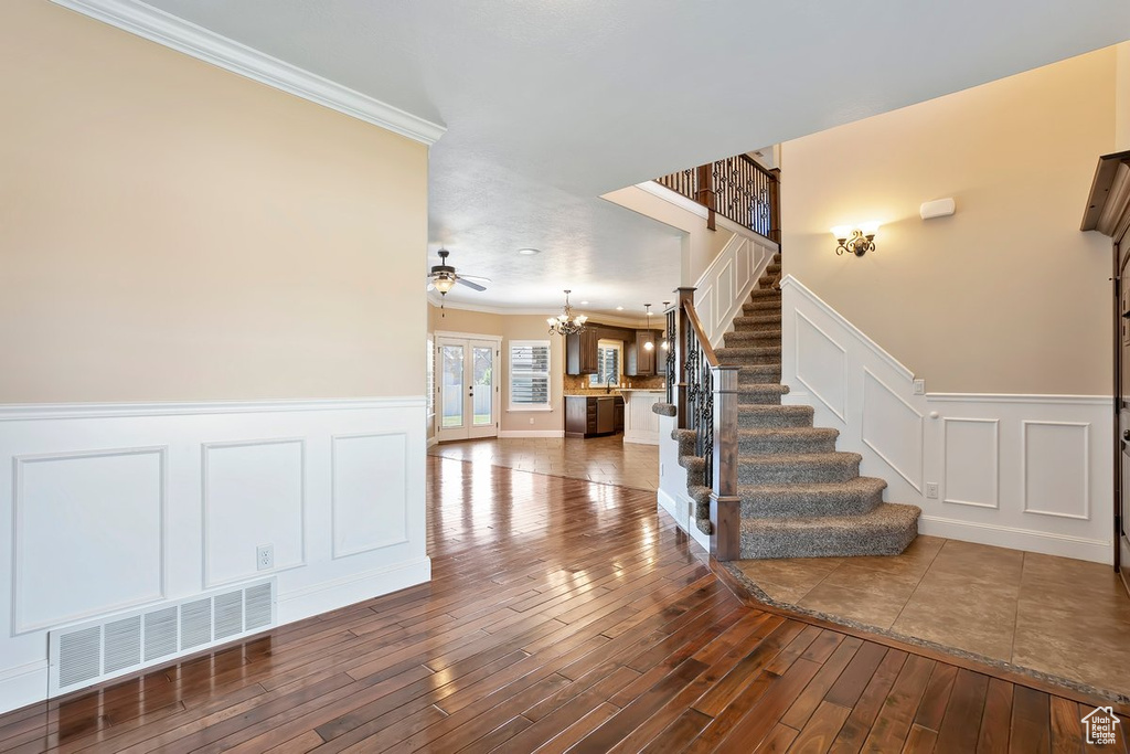 Staircase featuring ornamental molding, a chandelier, wood-type flooring, a decorative wall, and wainscoting