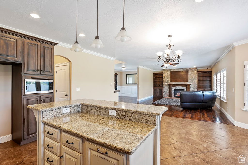 Kitchen with stainless steel microwave, built in features, light tile patterned floors, arched walkways, and light stone counters