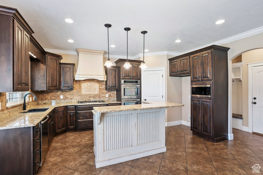 Kitchen with custom exhaust hood, stainless steel appliances, dark brown cabinetry, arched walkways, and recessed lighting