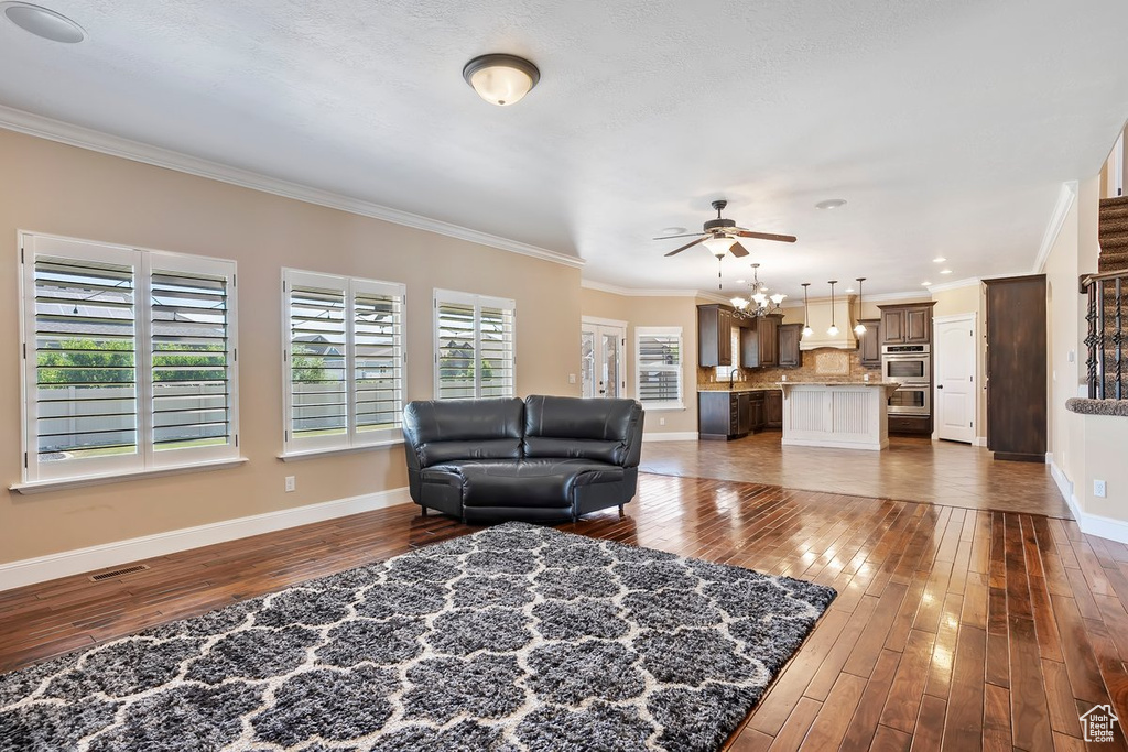 Living area featuring crown molding, dark wood-style floors, and a ceiling fan