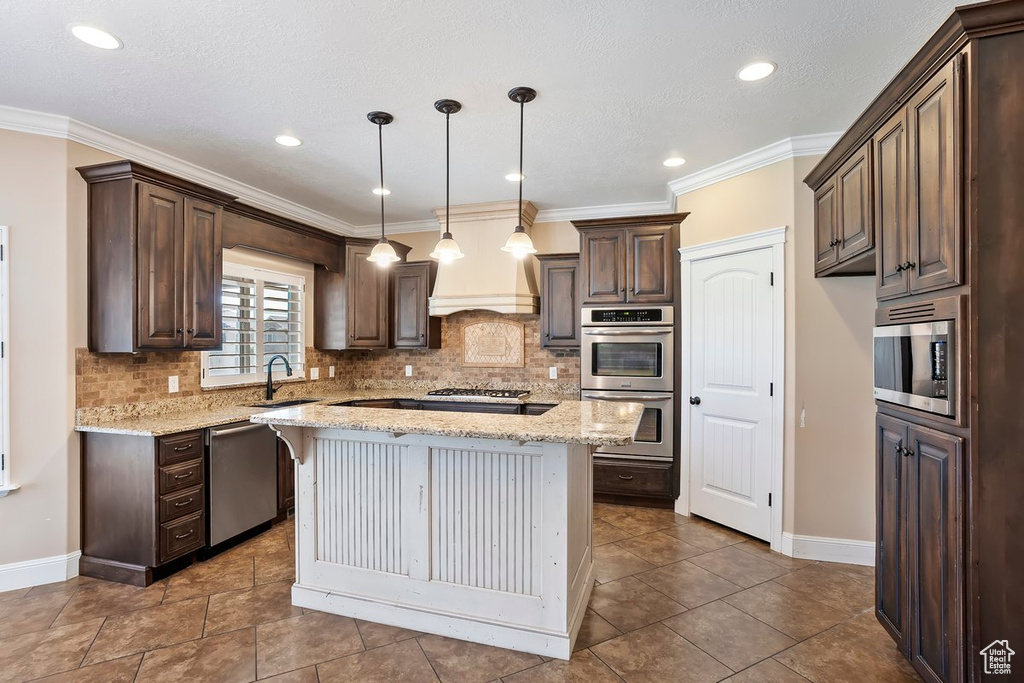 Kitchen featuring stainless steel appliances, dark brown cabinetry, a center island, tasteful backsplash, and light stone counters