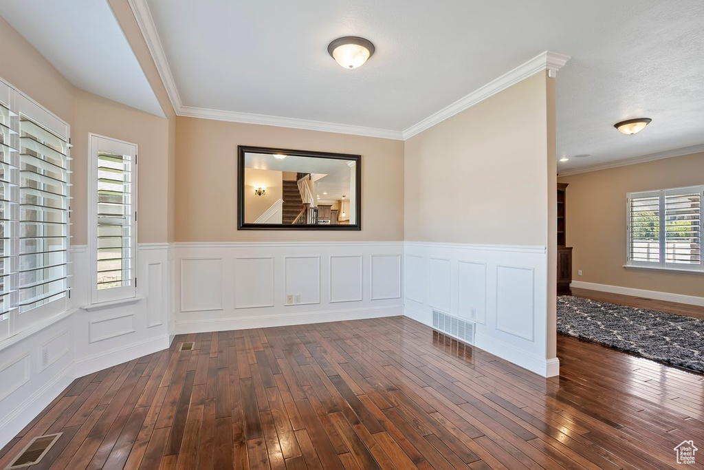 Unfurnished room featuring dark wood finished floors, wainscoting, and crown molding
