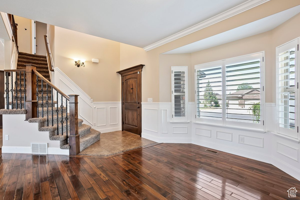 Entryway featuring hardwood / wood-style flooring, a decorative wall, wainscoting, stairs, and crown molding