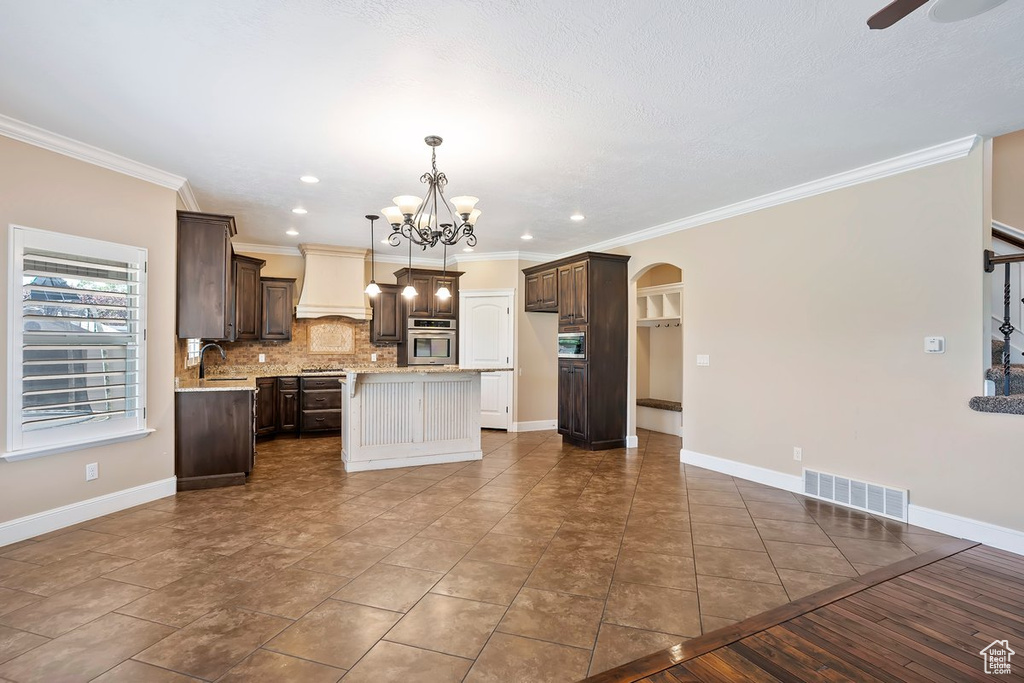 Kitchen featuring custom range hood, arched walkways, dark brown cabinets, a kitchen island, and crown molding