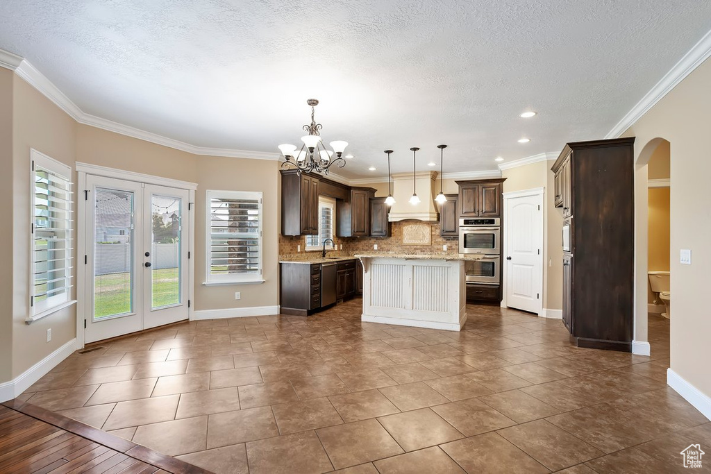 Kitchen with arched walkways, a kitchen island, decorative backsplash, a chandelier, and dark brown cabinets
