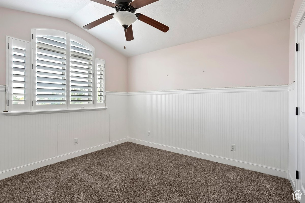 Carpeted spare room featuring a wainscoted wall, ceiling fan, and lofted ceiling
