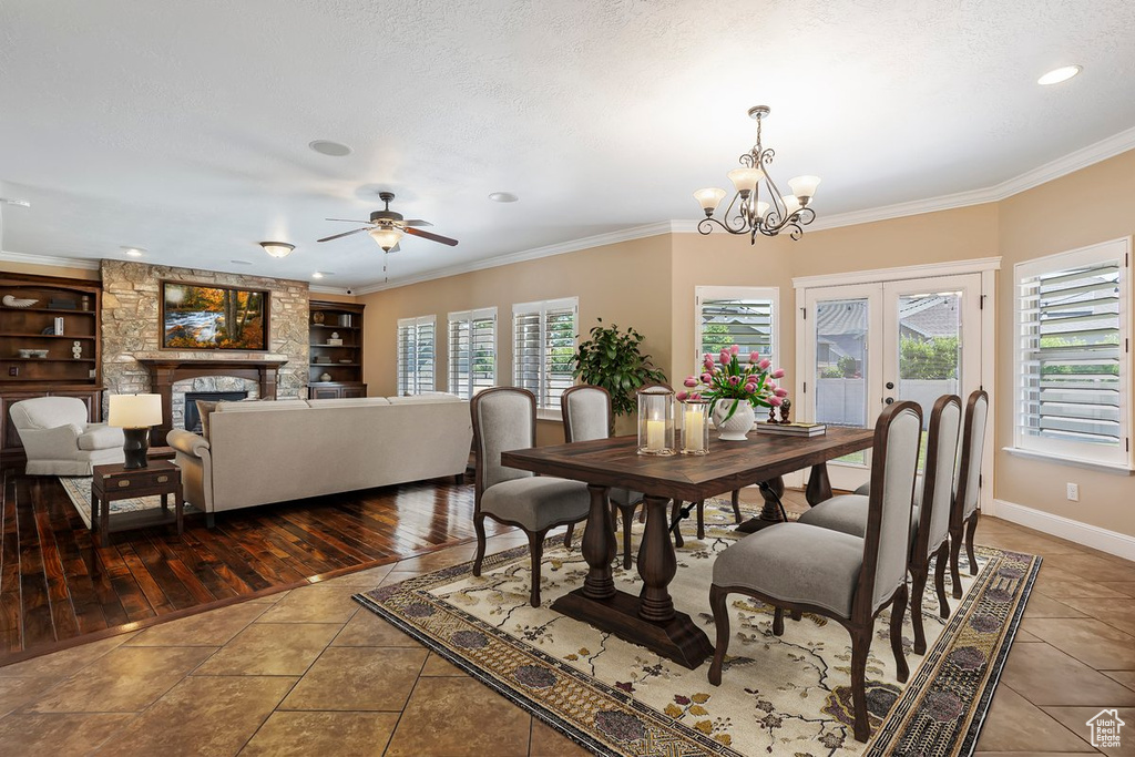 Tiled dining space with a ceiling fan, ornamental molding, a stone fireplace, a chandelier, and built in features