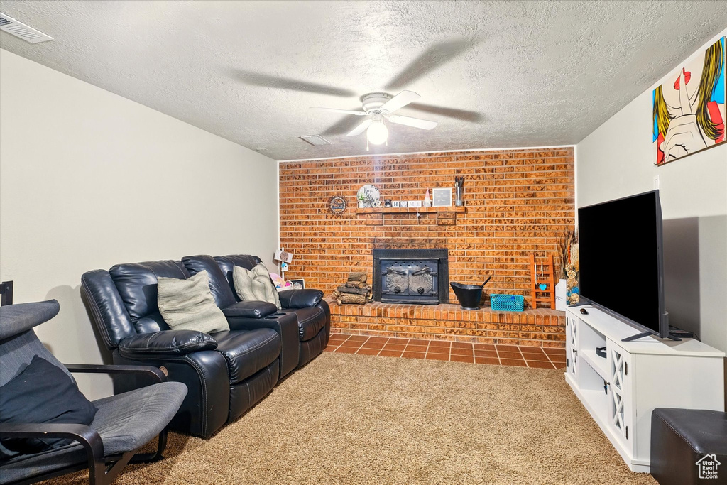 Living room with carpet floors, ceiling fan, a fireplace, and a textured ceiling