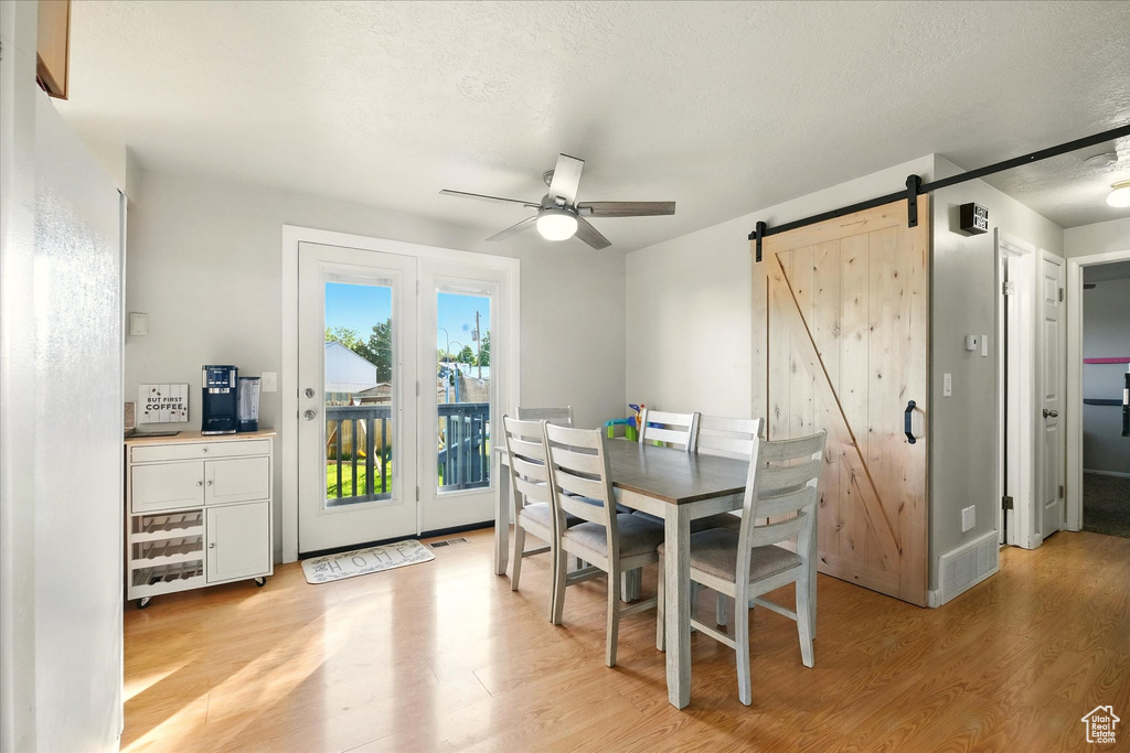 Dining space featuring a barn door, light wood-type flooring, ceiling fan, and a textured ceiling