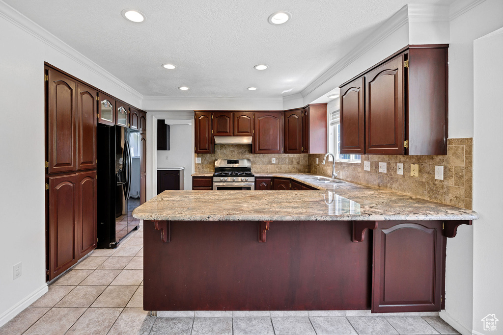 Kitchen with gas stove, black refrigerator with ice dispenser, a peninsula, under cabinet range hood, and decorative backsplash