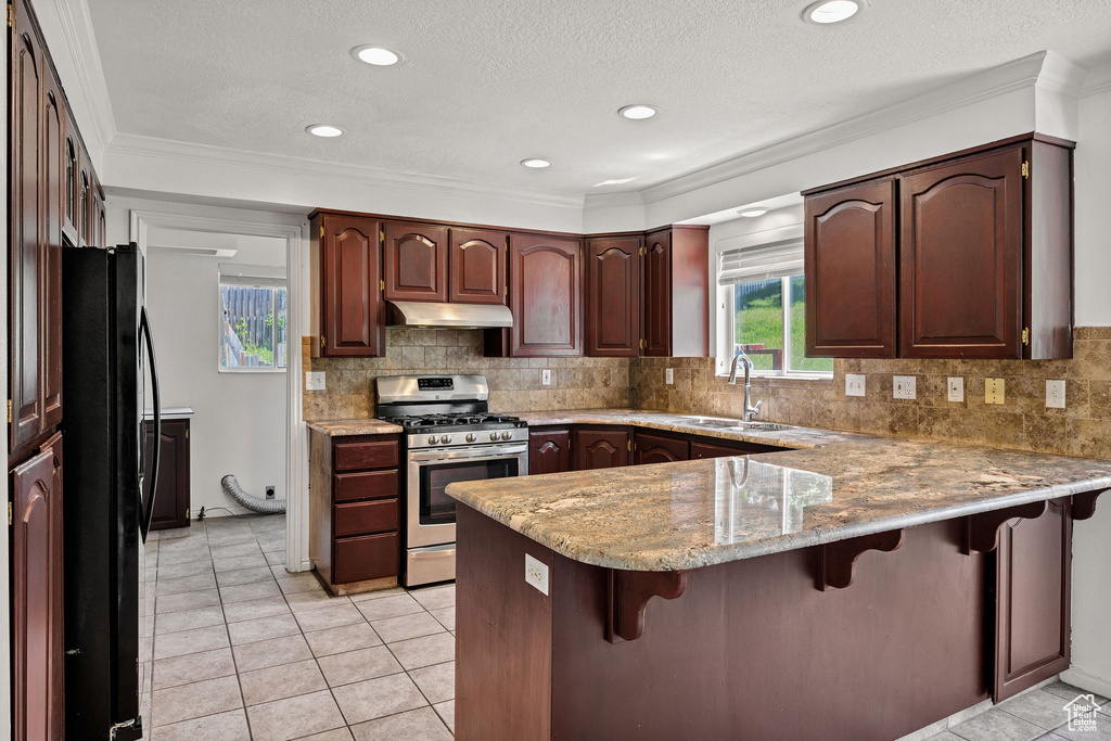 Kitchen featuring stainless steel gas range oven, under cabinet range hood, a peninsula, freestanding refrigerator, and a breakfast bar area