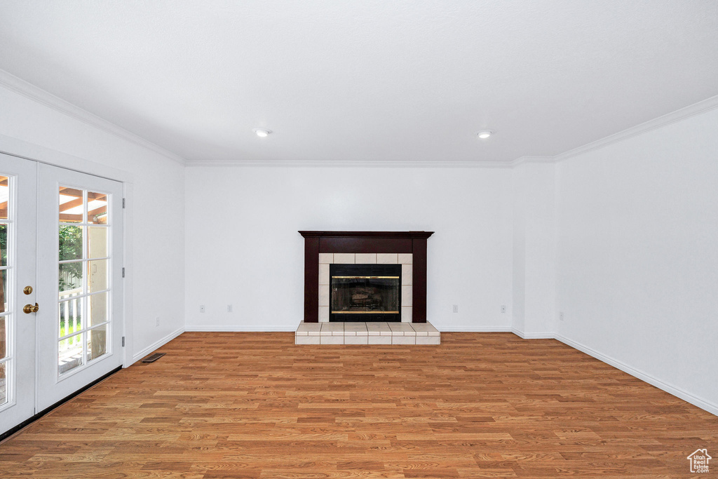 Unfurnished living room with ornamental molding, light wood-style floors, french doors, a tiled fireplace, and recessed lighting