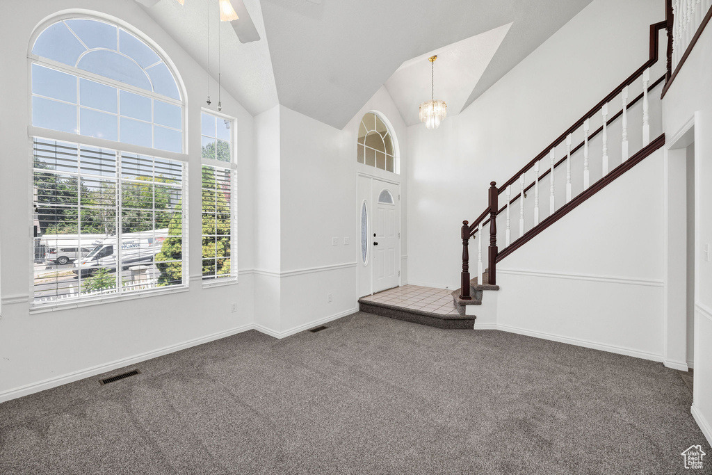 Carpeted entryway featuring a chandelier, vaulted ceiling, a ceiling fan, and stairway