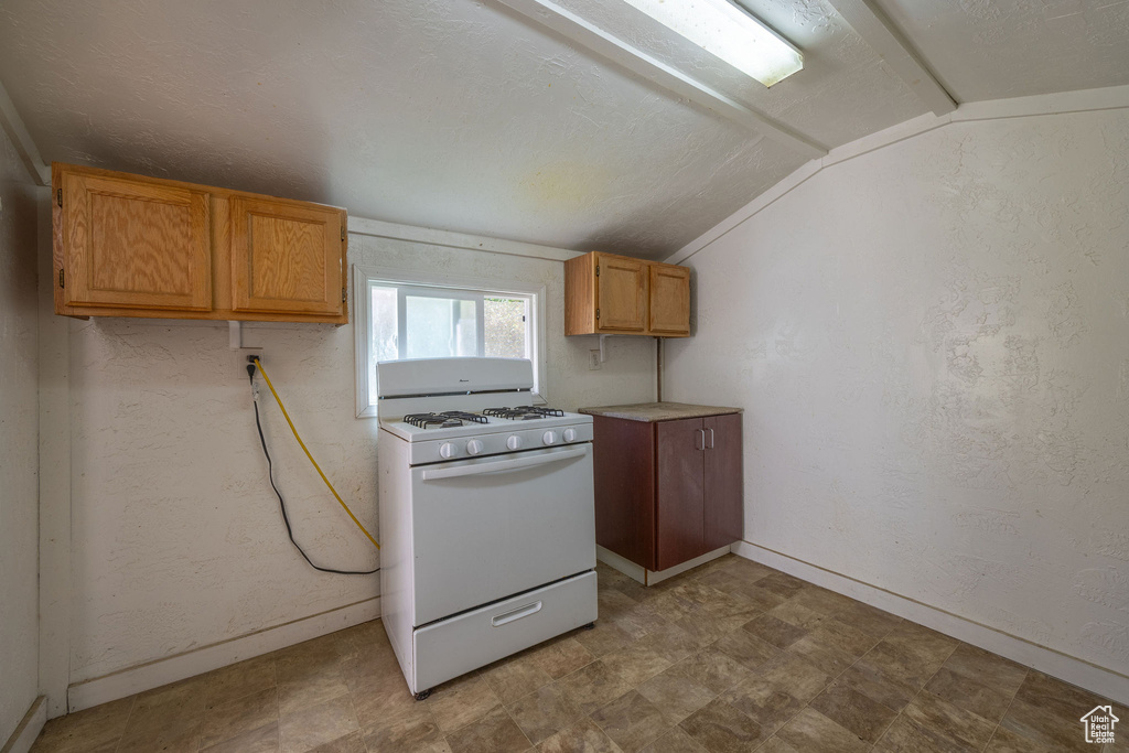 Kitchen featuring white range with gas cooktop, vaulted ceiling, and light countertops