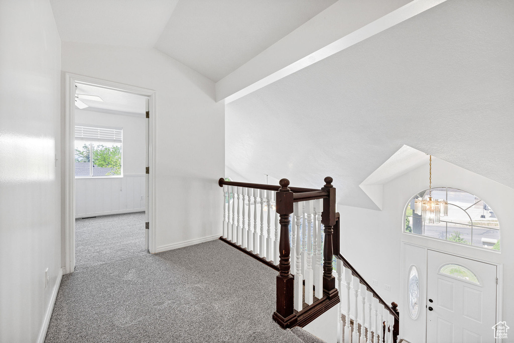 Hall featuring a chandelier, carpet, vaulted ceiling, and an upstairs landing