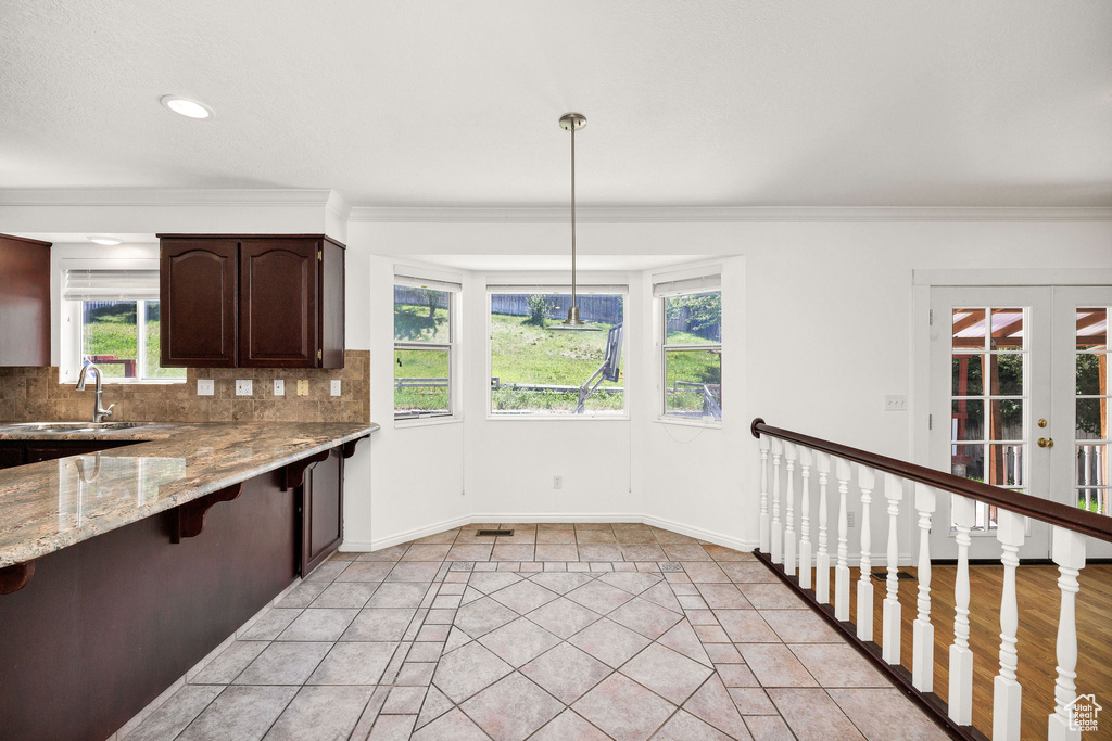 Kitchen featuring dark brown cabinetry, light stone countertops, a kitchen breakfast bar, ornamental molding, and decorative backsplash