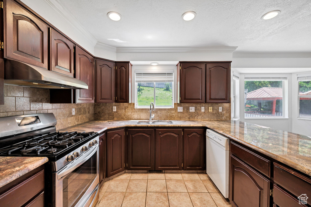 Kitchen featuring stainless steel range with gas stovetop, under cabinet range hood, white dishwasher, ornamental molding, and backsplash