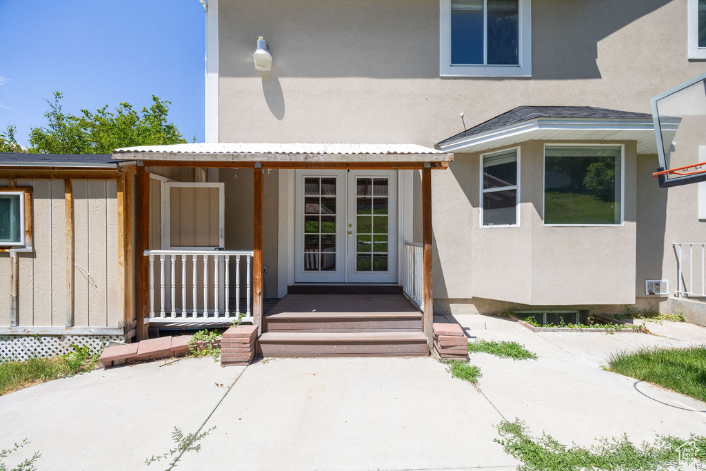 View of exterior entry featuring french doors, stucco siding, and covered porch