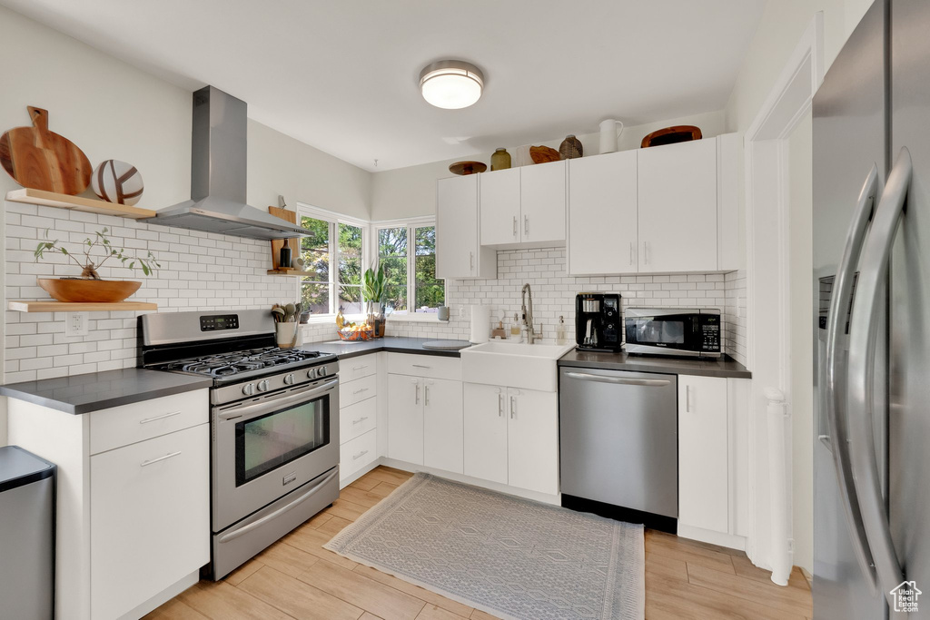 Kitchen with appliances with stainless steel finishes, open shelves, wall chimney exhaust hood, dark countertops, and backsplash