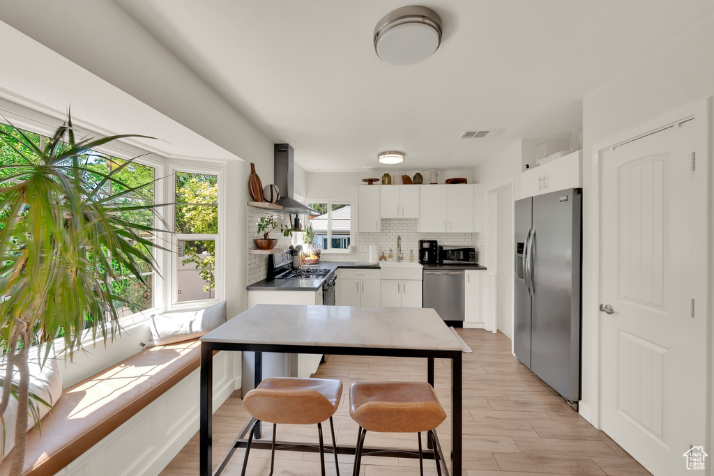 Kitchen with appliances with stainless steel finishes, wall chimney range hood, backsplash, a sink, and white cabinetry