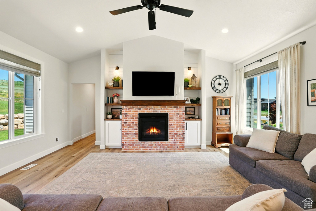Living area with vaulted ceiling, a brick fireplace, light wood-style flooring, ceiling fan, and recessed lighting
