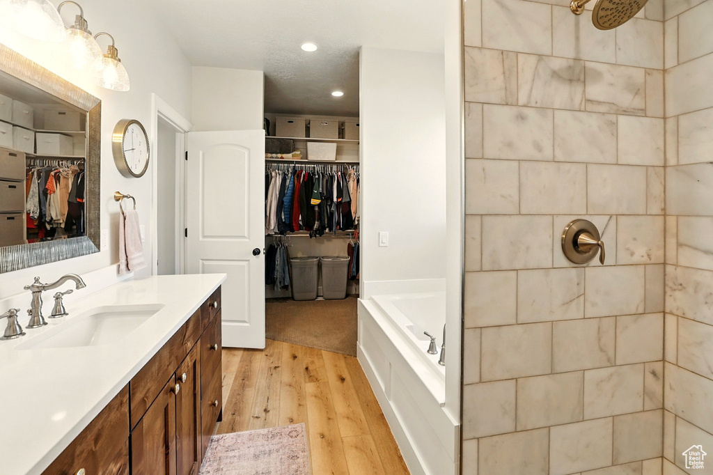 Full bath with wood finished floors, vanity, a walk in closet, tiled shower, and recessed lighting