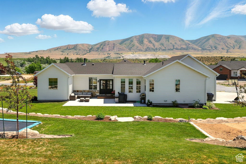 Back of property with an outdoor living space, a patio, a mountain view, a trampoline, and a lawn