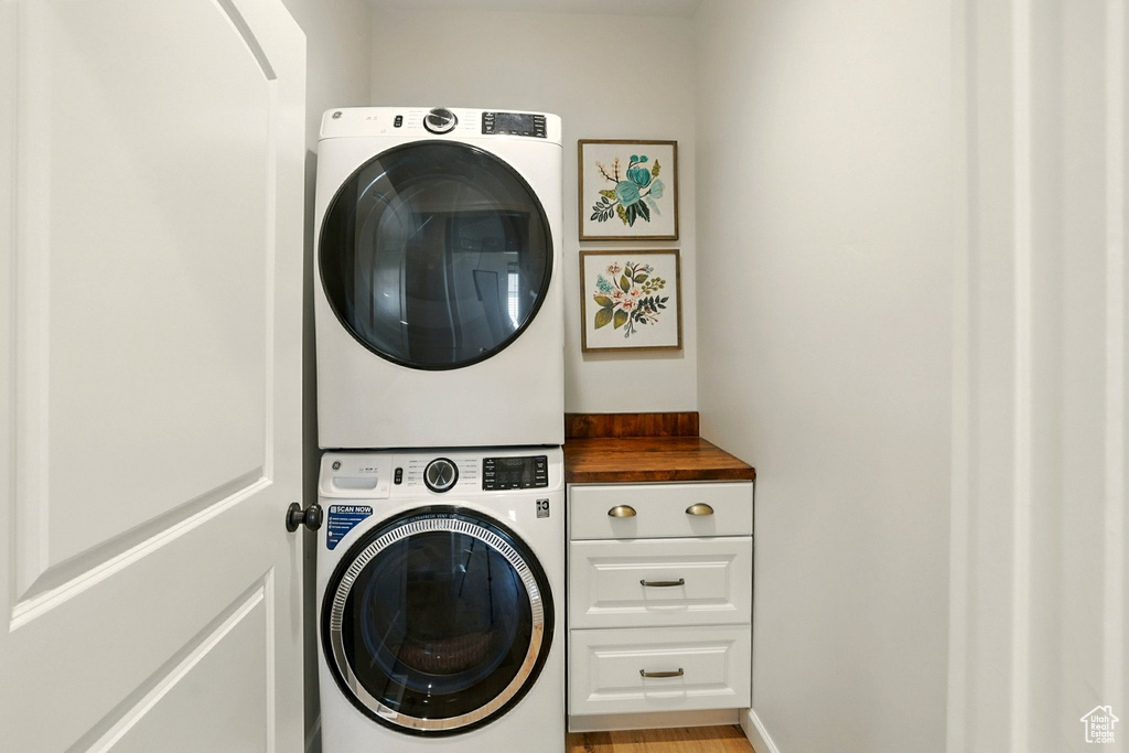 Laundry room featuring stacked washer and clothes dryer, cabinet space, and light wood finished floors