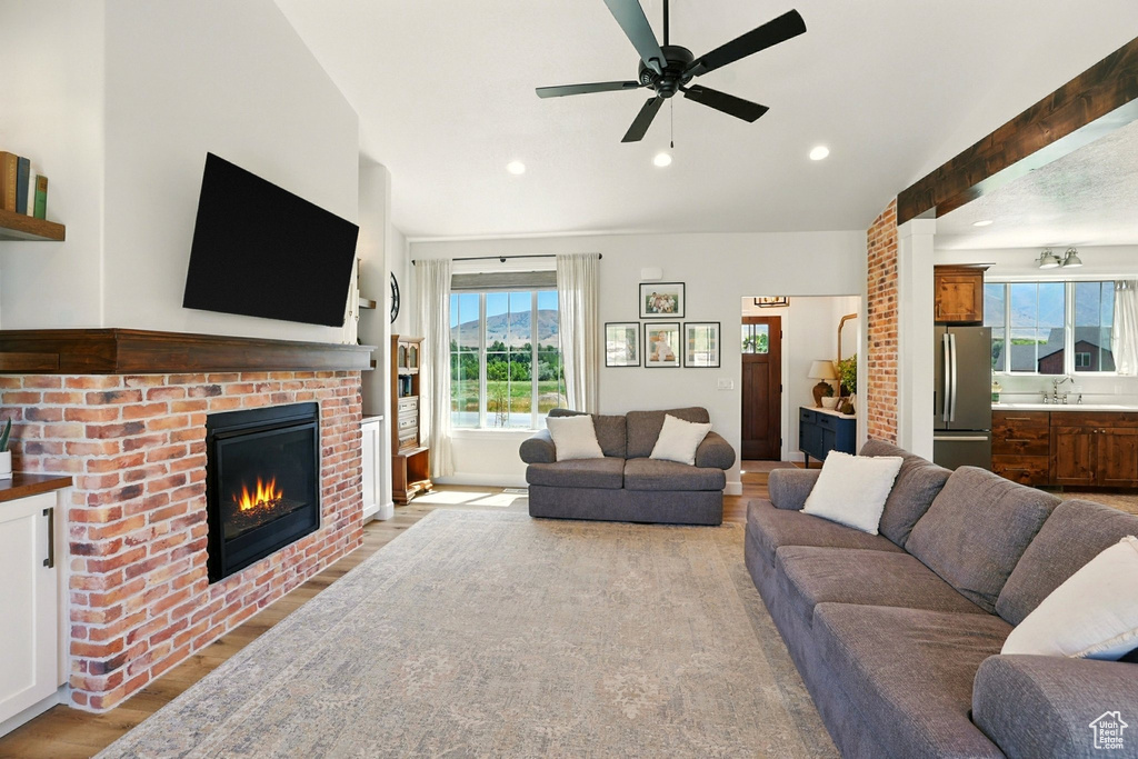 Living area featuring light wood-style floors, ceiling fan, a fireplace, recessed lighting, and vaulted ceiling