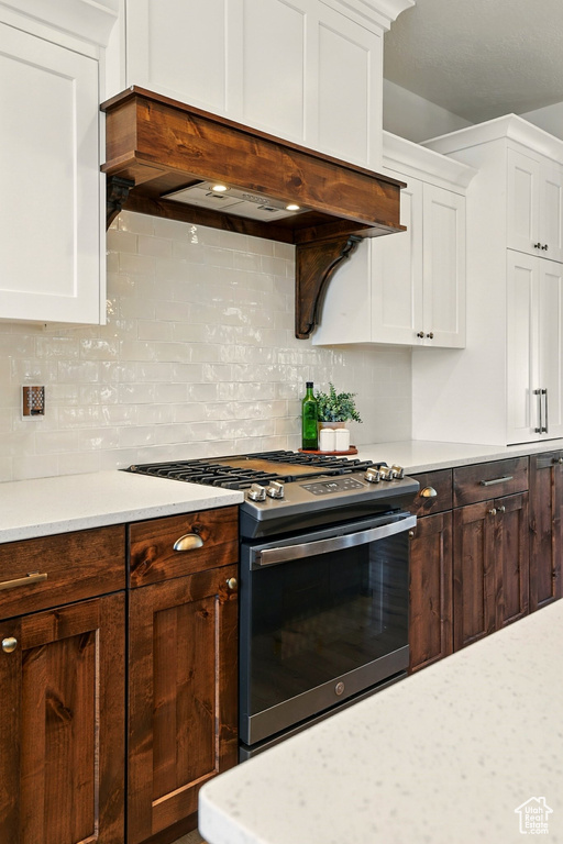 Kitchen with gas stove, light countertops, custom exhaust hood, and white cabinets