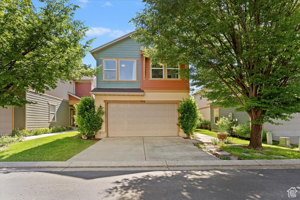 Traditional home featuring a garage, driveway, stucco siding, and a front yard