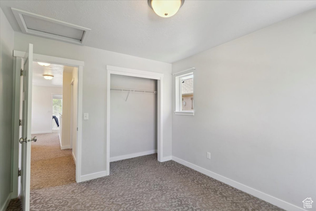 Unfurnished bedroom featuring carpet flooring, attic access, and a closet