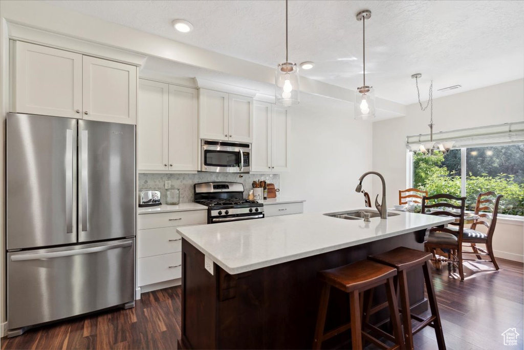 Kitchen featuring appliances with stainless steel finishes, decorative backsplash, dark wood-style floors, light countertops, and an island with sink