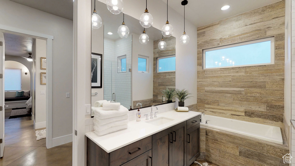 Ensuite bathroom with plenty of natural light, tiled tub, vanity, and a ceiling fan