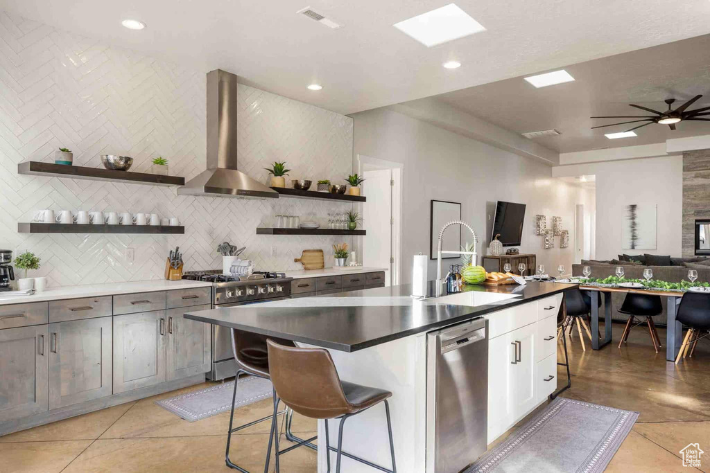 Kitchen with stainless steel appliances, wall chimney exhaust hood, open shelves, open floor plan, and tasteful backsplash
