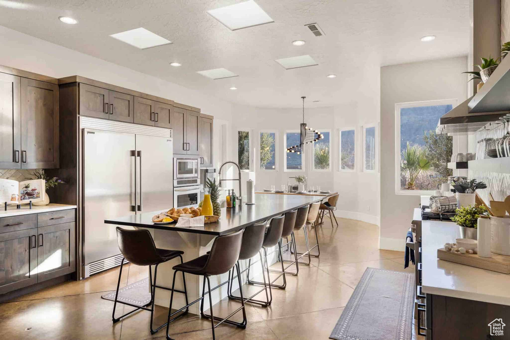 Kitchen with built in appliances, a kitchen breakfast bar, dark brown cabinets, decorative backsplash, and recessed lighting