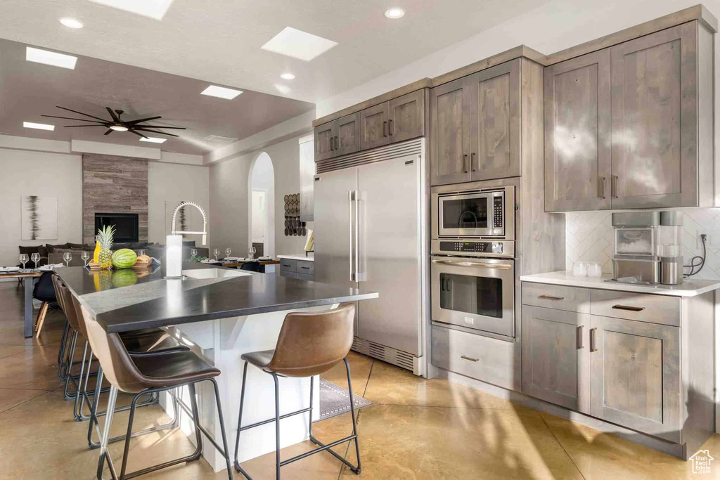 Kitchen featuring built in appliances, arched walkways, finished concrete floors, a ceiling fan, and tasteful backsplash