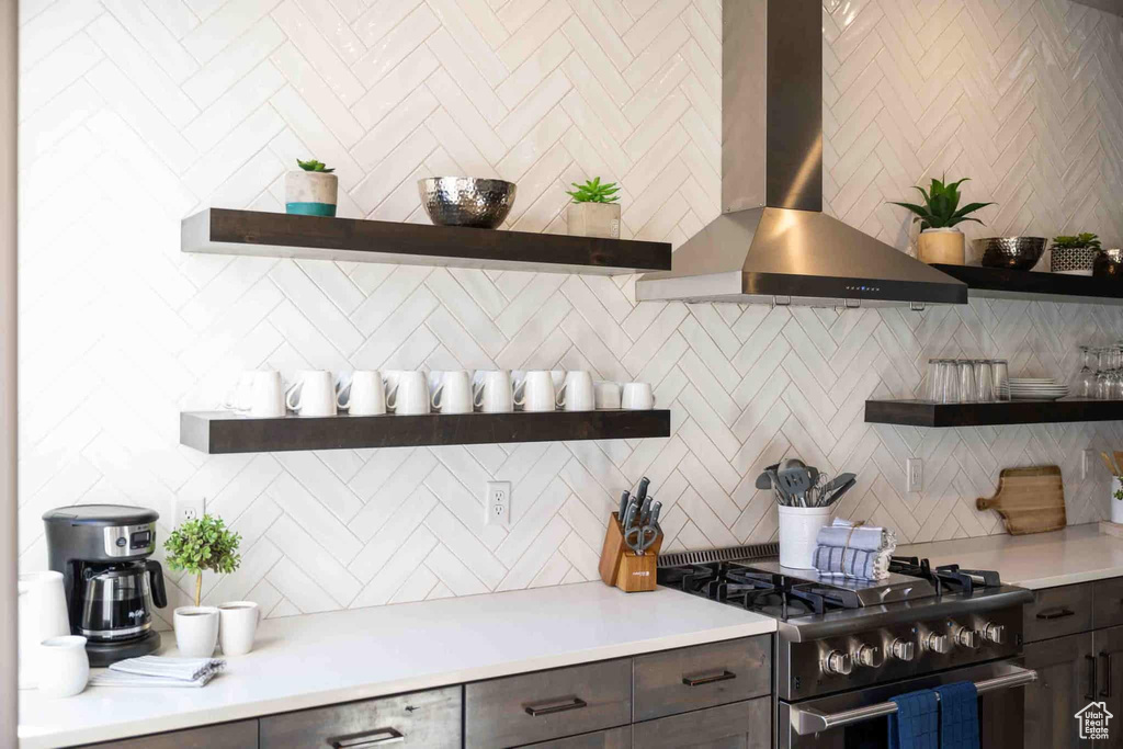 Kitchen with open shelves, stainless steel range with gas cooktop, exhaust hood, backsplash, and light countertops