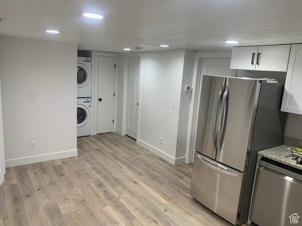 Kitchen featuring stainless steel appliances, stacked washer / drying machine, white cabinetry, light wood finished floors, and recessed lighting