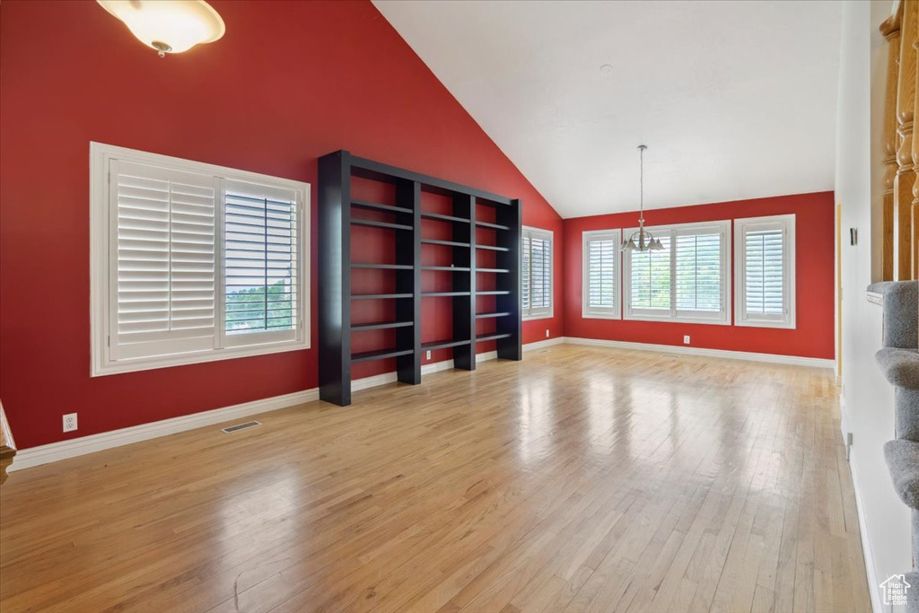 Unfurnished living room featuring plenty of natural light, wood finished floors, a chandelier, baseboards, and high vaulted ceiling